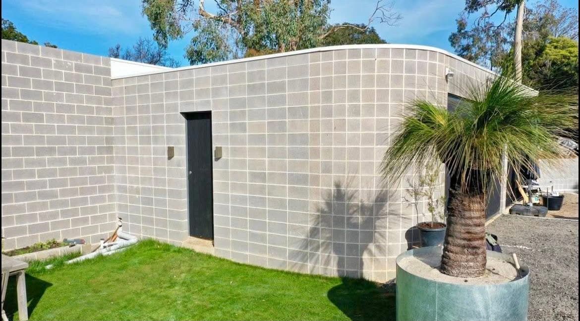 Finished curved grey-block building wall with smooth radius corner. Every block hand-laid by eye, no string lines, no set-out templates. Ash Huskisson Masonry.