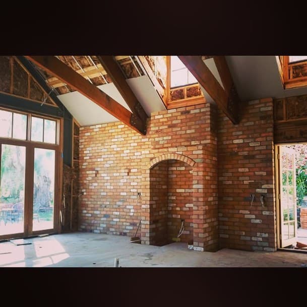 Interior with hand-laid red-brick archway and feature wall under exposed timber rafters. Recent work.
